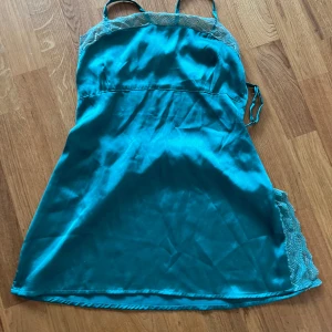 Grön linnetopp med spets och öppen rygg - Säljer en grön linnetopp med tunna axelband och spetsdetalj upptill. Toppen har en öppen rygg med korsade band och en lätt glansig finish. Perfekt för varma dagar eller sommarens alla tillfällen.