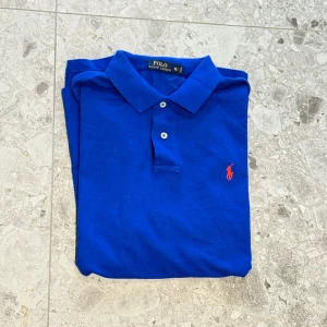 Blå pikétröja från Polo Ralph Lauren - Säljer en klassisk blå pikétröja från Polo Ralph Lauren med korta ärmar och krage. Nypriset ligger på ca 1500kr