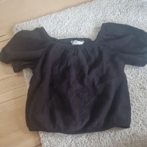 Svart croppad topp med puffärmar från H&M - Säljer en svart croppad topp från H&M med puffiga korta ärmar och resår vid halsringningen. Toppen har en luftig och trendig passform som passar perfekt till jeans eller kjol.