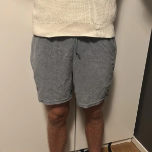 Grå frottéshorts med snörning - Mysiga grå shorts i mjuk frotté med elastisk midja och snörning framtill. De har en avslappnad passform och sidofickor, perfekta för chill dagar eller när du vill ha det bekvämt. Enkla att matcha med t-shirt eller hoodie. Storlek M och passar även bra på S.