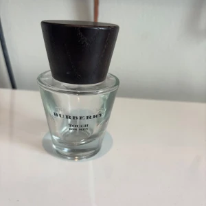Burberry Touch For Men parfym (tom flaska) - Stilren parfymflaska från Burberry Touch For Men med transparent glas och en stor, mörkbrun träkork. Flaskan har en konisk form och minimalistisk design med svart text. Perfekt för dig som gillar klassiska och eleganta dofter.