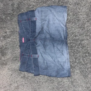 Jeanskjol med detaljer från Replay - Snygg kort jeanskjol från Replay i klassisk blå denim. Kjolen har  bältesdetaljer med röda sömmar och knappar i midjan. På bilderna ser jeansen gråa pga av ljuset ut men dem har egentligen en klassisk jeansblå färg. Om ni är intresserade kan ni be om fler bilder.💗