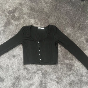 Svart ribbad topp från NA-KD - Säljer en svart croppad topp från NA-KD med lång ärm och snygg ribbad struktur. Säljer då den aldrig kommit till användning💕💕