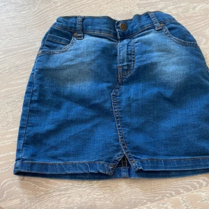 Blå jeanskjol från A denim story - Snygg blå jeanskjol från A denim story med klassisk femficksdesign, knapp och dragkedja framtill samt liten slits. Kjolen har resår i midjan bak och coola slitningar för en avslappnad look. Perfekt till sneakers eller boots.