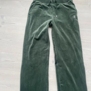 Juicy Couture gröna velourbyxor XS - Mörkgröna mjukisbyxor från Juicy Couture i velour med dragsko i midjan och fickor. Snygg strasslogga på höften och stor Juicy-text i strass bak. Perfekta för en chill och trendig look. Helt nytt skick.