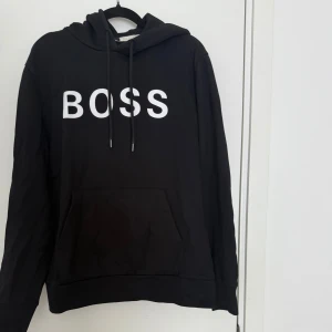 Svart hoodie från BOSS med tryck - Svart hoodie från BOSS med vit text på bröstet. 