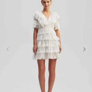 Vit spetsklänning med volanger - Superfin vit miniklänning i spets med flera lager volanger och v-ringning. perfekt för student eller sommarens speciella tillfällen. Söt och trendig look med mycket volym och detaljer❤️ nypris 2800