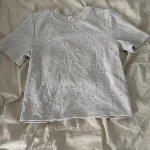 Ljus stickad topp med pärlor från Zara - Superfin ljus stickad topp från Zara med korta ärmar och rund hals. Toppen är dekorerad med små pärlor över hela framsidan. Tröjan är aldrig använd. Passar även de med strl xs 