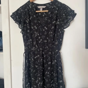 Svart blommig klänning H&M - Supersöt svart klänning från H&M med små vita blommor, v-ringning och volangärmar. Klänningen har resår i midjan och knytband i sidorna. Aldrig använd💛