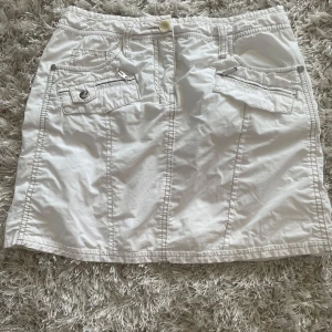 Vit kortkjol från Esprit med fickor - Snygg vit kortkjol från Esprit med coola detaljer som dragkedjor och knappar på fickorna. Kjolen har flera praktiska fickor både fram och bak samt bälteshällor. Passar även S