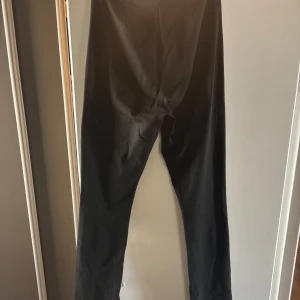 Svarta slim byxor med slits  - Svarta byxor med slim passform och raka ben. Snygg minimalistisk look som passar till det mesta. Materialet ser ut att vara bomull eller en bomullsblandning. Perfekta för dig som gillar stilrena och enkla plagg.