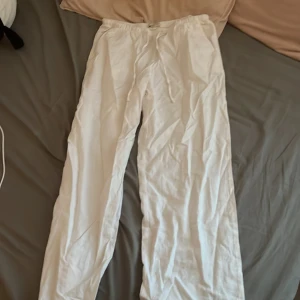 Vita linnebyxor från Gina Tricot - Säljer ett par vita linnebyxor, lågmidjade. från Gina Tricot i storlek M. Byxorna har rak passform, resår i midjan och snörning för extra komfort. Perfekta för chill dagar eller när du vill ha en clean och luftig look.