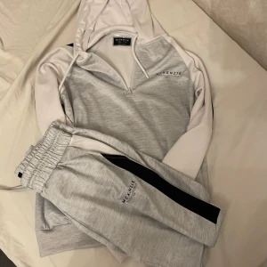 Grå hoodie från McKenzie med half zip - Snygg ljusgrå hoodie från McKenzie med vita ärmar och svarta detaljer på axlarna. Tröjan har huva med snörning, half zip och lång ärm. Perfekt för chill dagar eller träning. Materialet är mjukt och känns sportigt. Jag har använt den en gång. Den är för liten.