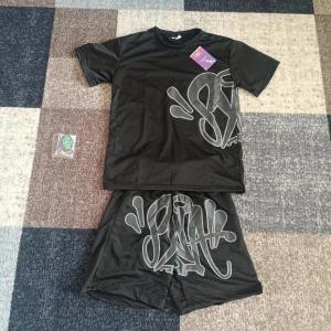 Syna world set - Svart t-shirt från syna world med stort grått graffiti-inspirerat tryck på både fram- och baksidan. T-shirten har rund hals och korta ärmar. Perfekt för dig som gillar streetwear och vill sticka ut.