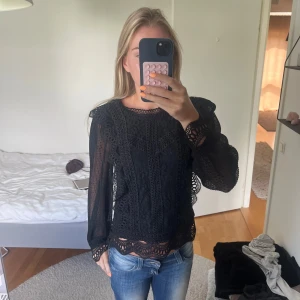 Svart spetsblus med lång ärm - Säljer en svart blus med vackra spetsdetaljer och lång ärm. Blusen har genombruten design, rund halsringning och fina broderade kanter vid ärmslut och nederkant. Perfekt för dig som gillar romantisk och trendig stil.