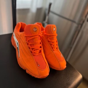 Orange sneakers från Li-Ning - Färgstarka sneakers från Li-Ning i en intensiv orange nyans med silvriga detaljer på sidorna och hälen. Skorna har snörning, mesh och syntetmaterial samt en chunky sula. Perfekta för dig som vill sticka ut med din stil.