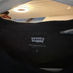Svart Levi's t-shirt med logga - Svart t-shirt från Levi's i bomull med klassisk stor logga framtill i blått, vitt och rött. T-shirten har rund halsringning och korta ärmar. Perfekt för en avslappnad och cool stil.