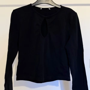 Svart långärmad topp med nyckelhåls hals - Svart långärmad topp med en snygg droppformad öppning vid halsen. Enkel och stilren, perfekt till både fest och vardags. Normal passform och rund halsringning. Lappen är avklippt men är inget som märks av, den skavde en del innan.