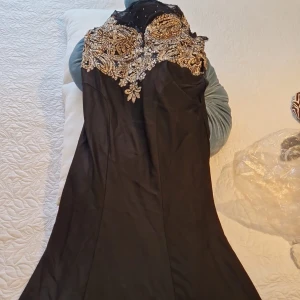 Svart långklänning med guldpaljetter - Säljer en svart långklänning med lyxiga guldfärgade paljetter och broderier upptill. Klänningen har mesh vid axlarna och korta ärmar, samt en elegant figurnära passform. Perfekt för bal eller festkvällar när du vill sticka ut.