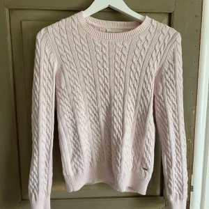 Ljusrosa kabelstickad tröja Holly & Whyte - Supersöt ljusrosa kabelstickad tröja från Holly & Whyte by Lindex. Tröjan har rund hals, långa ärmar och en snygg ribbad kant vid ärmslut och nederkant. Perfekt för lager-på-lager och chill dagar. Metallbricka med logga nertill. 