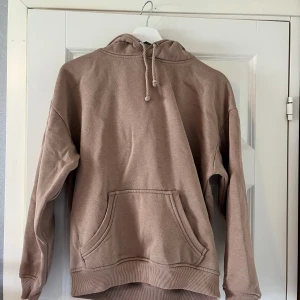 Beige hoodie från bikbok  - Säljer en beige hoodie med klassisk känguruficka och dragsko i huvan. Tröjan har ribbade muddar vid ärmslut och nederkant, samt en avslappnad passform. Perfekt för chill dagar eller när du vill ha något bekvämt och stilrent. Oversized passform.