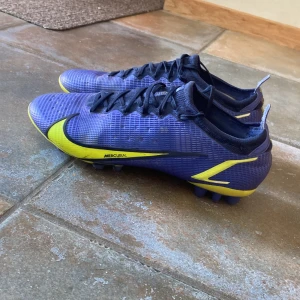 Nike Mercurial blå fotbollsskor - Säljer ett par Nike Mercurial fotbollsskor i blått med snygga gula detaljer och svart Nike-logga. Säljer dom för att det var några år sedan jag slutade med fotbollen, så dom har helt enkelt blivit bort glömda
