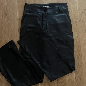 Svarta skinnbyxor från Madlady - Snygga svarta byxor i skinnimitation från Madlady. De har raka ben, klassisk midja och stängs med knapp och dragkedja. Perfekta för dig som vill ha en edgy look och gillar trendiga material. Passar till allt från sneakers till boots.