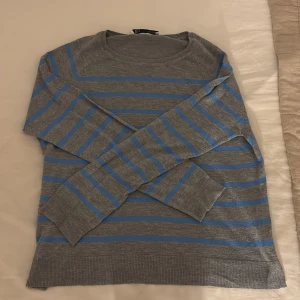 Gråblå randig långärmad tröja - Snygg grå tröja med blå ränder och rund hals. Långärmad modell med ribbade muddar vid ärmslut och nederkant. Perfekt för dig som gillar en enkel men stilren look. Passar till jeans. 