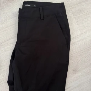 Svarta lågmidjade kostymbyxor med slits från BikBok - Svarta snygga kostymbyxor från Bikbok, med låg midja och slits nertill. Passar perfekt för en clean och stilren look till vardagen men också till fest!. Materialet känns mjukt och följsamt. Använda ett fårtal gånger men inga fläckar eller hål🤍Modellen är Vera och i storlek 38💞💞