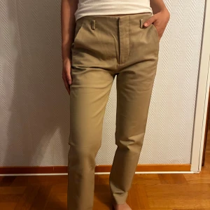 Beige kostymbyxor från Zara Basic - Snygga beige kostymbyxor från Zara Basic i rak modell med hög midja. Byxorna har hällor för bälte, diskreta fickor bak och är tillverkade i ett mjukt bomullsmaterial. Perfekta för en clean och stilren look.