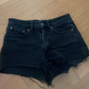 Svarta jeansshorts med fransig kant - Svarta jeansshorts i klassisk femficksmodell med rå, fransig kant nertill. Hög midja och dragkedja med knapp framtill. Perfekta för sommaren och riktigt snygga till sneakers eller boots.