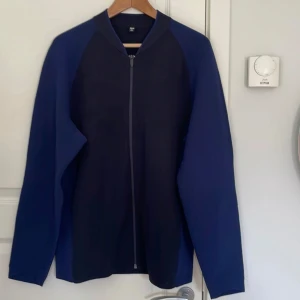 Mörkblå bomberjacka från Uniqlo. Helt ny. - Snygg mörkblå bomberjacka från Uniqlo med hel dragkedja framtill. Jackan har ribbad krage och är tillverkad i ett mjukt, stickat material. Perfekt för dig som gillar en clean och stilren look. Passar till många olika outfits och är riktigt bekväm.