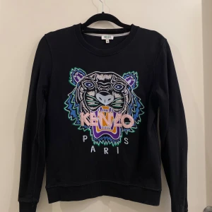 Svart Kenzo sweatshirt - Svart sweatshirt från Kenzo med ikonisk broderad tiger i flera färger på bröstet och Kenzo Paris-text. Tröjan har rund hals, långa ärmar och ribbade muddar.