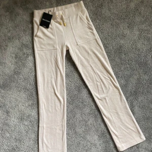 Beiga mjukisbyxor Juicy Couture XXS - Superfräscha beiga mjukisbyxor från Juicy Couture med raka ben, stora fickor fram och bak samt gulddetaljer på snörningen. Broderad JC-logga framtill. Perfekta för en chill och trendig look. Helt oanvända med lappen kvar där av priset!