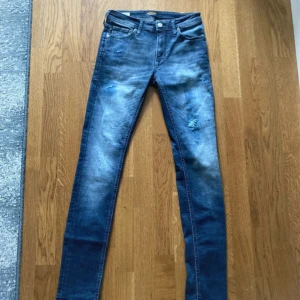 Blå jeans/slim fit från Jack & Jones - Snygga blå skinny jeans från Jack & Jones med slitna detaljer och tvättad look. Klassisk femficksmodell med normal midja och stretchigt denimtyg för skön passform. Perfekta för dig som gillar en smal siluett och lite ruff vibe. Storlek 28/32. Priset kan diskuteras