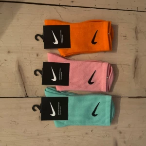 Nike färgglada ribbade strumpor - Tre par ribbade strumpor från Nike i orange, rosa och turkos med svart Nike-logga på sidan. Perfekta för att liva upp outfiten och ge en sportig vibe. Snygga färger som sticker ut och passar till sneakers eller träning.