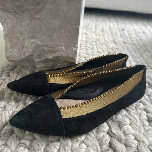 Svarta ballerinaskor med guldiga detaljer - Snygga ballerinaskor från Massimo Dutti i svart mocka med spetsig tå och guldigt band runt öppningen. Skorna har låg klack med gulddetalj och en elegant, modern look som sticker ut. 