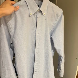 Ljusblå oxfordskjorta från Oscar Jacobson - Klassisk ljusblå oxfordskjorta i regular fit från Oscar Jacobson med button down-krage och vita knappar. Skjortan är långärmad och har en stilren, tidlös design i mjuk bomull. Perfekt för dig som gillar en clean och snygg look. Passar S/M använd 3 ggr
