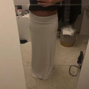Långkjol - Säljer en stilren vit långkjol med hög midja och rak passform. Kjolen är enkel och snygg, perfekt att matcha med crop tops eller stickade tröjor. Den har en mjuk och följsam känsla, vilket gör den superbekväm att bära.