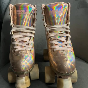 Holografiska rullskridskor från Impala - Snygga rullskridskor från Impala med holografisk, skimrande yta i rosa och silverton. Högt skaft, snörning och robust platt sula. Perfekta för dig som vill sticka ut på rinken eller gatan. Materialet är syntet och de har klassisk retrostil. Ny pris 1200.