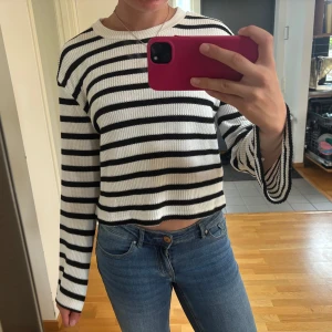 Randig stickad tröja från Gina Tricot - Säljer en vit och svart randig stickad tröja från Gina Tricot. Tröjan har en croppad passform, rund halsringning och långa ärmar. Materialet är mjukt och skönt, passar både till jeans och kjol.