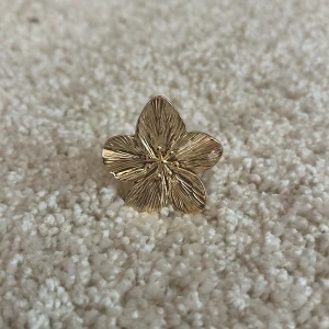 Guldig ring med stor blomma - Superfin statementring i guld med en stor, detaljerad blomma som motiv. Ringen har en bred ringbas och blomman har tydliga ådror och små prickar i mitten för extra effekt. Perfekt för dig som vill sticka ut med accessoarerna.