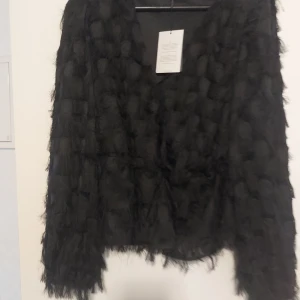 Svart v-ringad topp från JDY - Säljer en svart långärmad topp från JDY med v-ringning. Toppen har en unik textur med fluffiga detaljer och diskreta prickar som ger en cool look. Perfekt för dig som vill sticka ut lite extra. Modellen är normal i passformen.