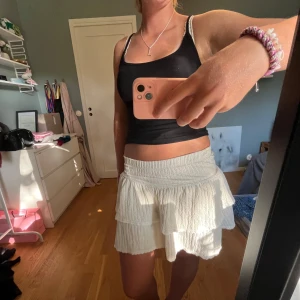 Vit volangkjol  - Supersöt vit kortkjol med volanger och bred resår i midjan. Kjolen har en luftig och lätt struktur, perfekt för varma dagar. Den är enkel att matcha och ger en fräsch vibe till din outfit. Bra skick. 