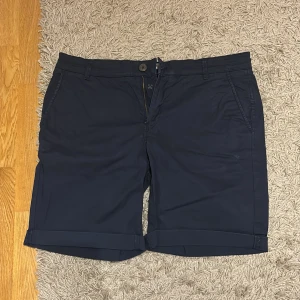 Mörkblå shorts från Selected Homme - Snygga mörkblå shorts från Selected Homme med klassisk passform. De har uppvikta benslut, sidofickor och bakfickor med knapp. Perfekta för sommaren och tillverkade i mjuk bomull för en bekväm känsla. Stilrena och lätta att matcha med det mesta.
