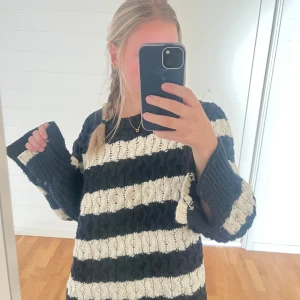 Randig stickad tröja i svart och vitt - Säljer en oversized stickad tröja med breda svarta och vita ränder. Tröjan har grov kabelstickning, rund hals och långa, vida ärmar.