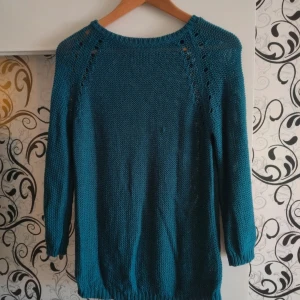 Petrolblå stickad tröja med håldetaljer - Säljer en petrolblå stickad tröja med snygga håldetaljer längs axlarna. Tröjan har rund halsringning, trekvartsärm och ribbade muddar vid ärmslut och nederkant. 
