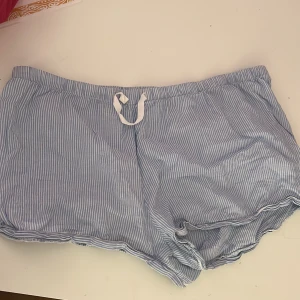 Blåvitrandiga pyjamas shorts - Säljer ett par blåvitrandiga shorts från H&M i mjuk bomull. De har snörning i midjan och avslappnad passform, perfekta för varma dagar. Klassisk look med tunna vertikala ränder och elastisk midja för extra komfort.
