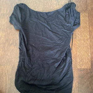 Svart topp med djup rygg Gina Tricot - En svart, enkel topp från Gina Tricot i mjuk bomull. Toppen har korta ärmar och en snygg djup urringning i ryggen med smal snörning upptill. Kom aldrig till användning och säljer därför den.