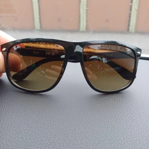 Ray-Ban svarta solglasögon Wayfarer - Snygga äkta Ray-Ban Wayfarer solglasögon med svart plastbåge och bruna tonade glas. Klassisk fyrkantig form och diskret Ray-Ban-logga på både lins och skalmar. Perfekta för att lyfta din stil under soliga dagar.